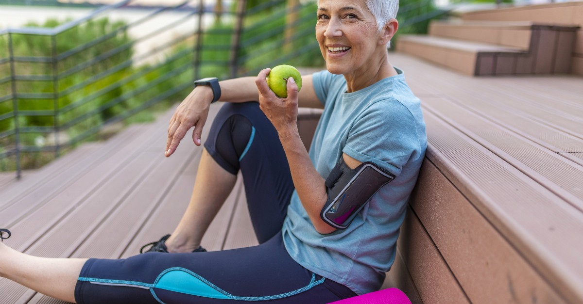 woman exercising outdoors, taking a break and eating an apple