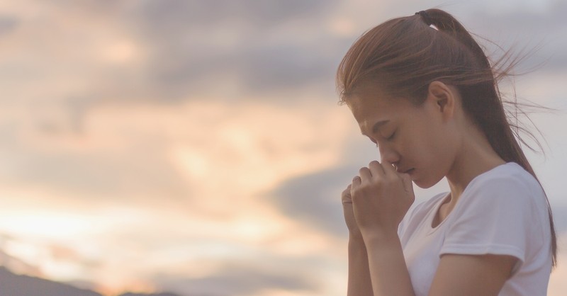 woman with head bowed praying outside, how to love an invisible God