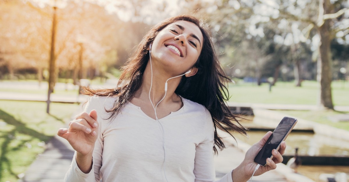 woman joyfully listening to music on headphones walking in park